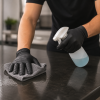 Persoon reinigt een werkblad met een microvezeldoek terwijl zwarte nitril handschoenen worden gedragen voor optimale hygiëne en bescherming.