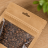 Detailopname van een kraft papieren stazak met transparant venster, gevuld met koffiebonen. De close-up toont het kijkvenster, de hoogwaardige afwerking en het ophanggat van de verpakking, waardoor de inhoud duidelijk zichtbaar is.
