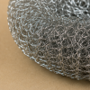 Macrodetail van een roestvrijstalen staalspons, waarbij de fijn gevlochten staaldraden en de stevige, slijtvaste structuur scherp zichtbaar zijn op een neutrale beige achtergrond.