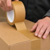 Detailfoto van bruine ECO papieren tape tijdens het sluiten van een kartonnen doos. De duurzame kraft tape wordt nauwkeurig aangebracht op de doosnaad, waarbij de sterke hechting en natuurlijke papierstructuur duidelijk zichtbaar zijn.