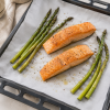 Wit gesiliconeerd bakpapier in gebruik op een bakplaat met ovengebakken zalmfilets en groene asperges, waarbij de hittebestendige anti-aanbakfunctie en veelzijdige toepassing van het bakpapier duidelijk worden getoond.