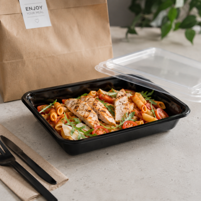 Zwarte PP thermo menuschaal 227 x 178 x 40 mm gevuld met pasta, gegrilde kip, cherrytomaten en rucola, gepresenteerd met transparant deksel, bestek en een afhaaltas als voorbeeld van gebruik voor maaltijdverpakkingen.