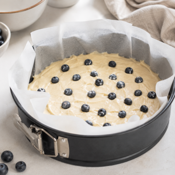 Bakpapier in gebruik in een ronde springvorm met cakebeslag en blauwe bessen, waarbij het witte gesiliconeerde bakpapier duidelijk zichtbaar is langs de randen voor een praktische toepassing in de keuken.