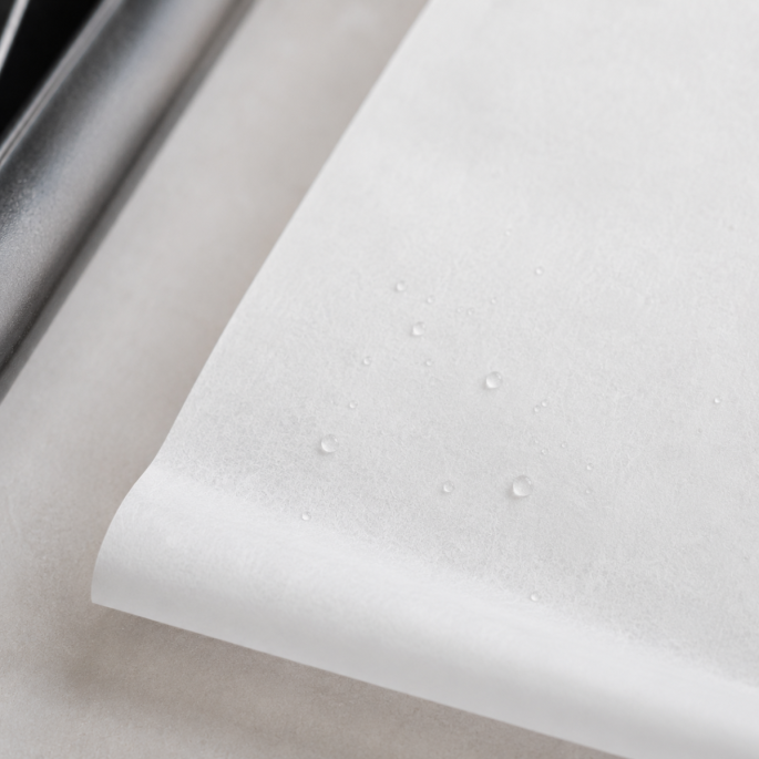 Gedetailleerde close-up van wit gesiliconeerd bakpapier met zichtbare waterdruppels op het oppervlak, waarmee de vochtbestendige anti-aanbakeigenschappen en fijne textuur van het papier worden benadrukt.